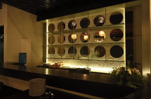 A modern bar area with a counter, a decorative wall with circular cutouts, and a water feature. - Hotel Vikram Palace (Varanasi)