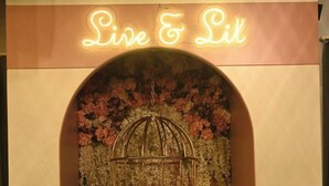 A seating area with a neon sign reading "Live & Lit," a hanging birdcage, and floral decorations. - Hotel Vikram Palace (Varanasi)
