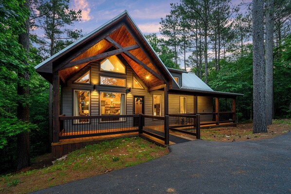 A log cabin with a large deck and multiple windows, surrounded by a forest. - New Honeymoon Cabin! King Bed, Hot Tub, 2 Fireplaces & Rain Shower (Broken Bow)