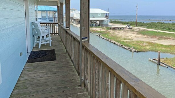 Une terrasse en bois offrant une vue sur l’eau et la plage, un espace salon abrité et un petit quai.