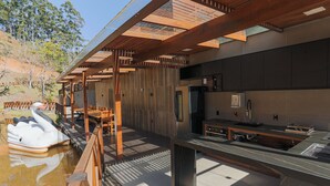 Un'area pranzo esterna moderna con travi in legno, una piscina con un galleggiante a forma di cigno e un bancone cucina.