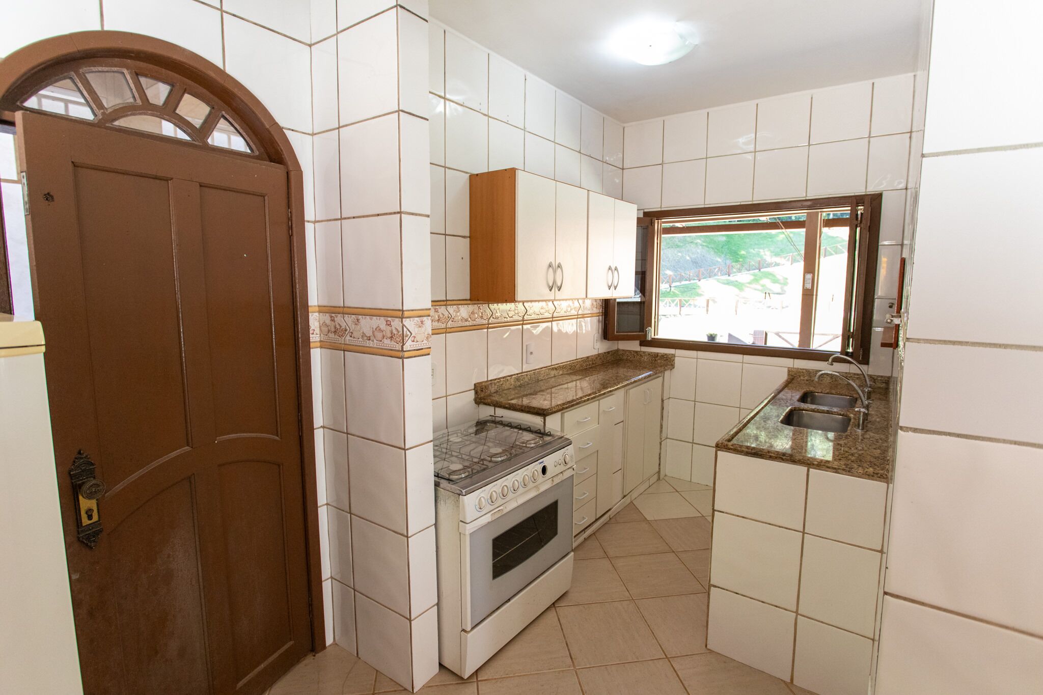 Una cucina con mobili bianchi, una porta marrone, un fornello e una finestra.