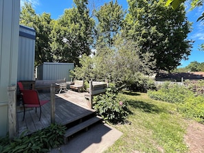 Una terraza de madera con mobiliario exterior, un pequeño jardín y un cobertizo.
