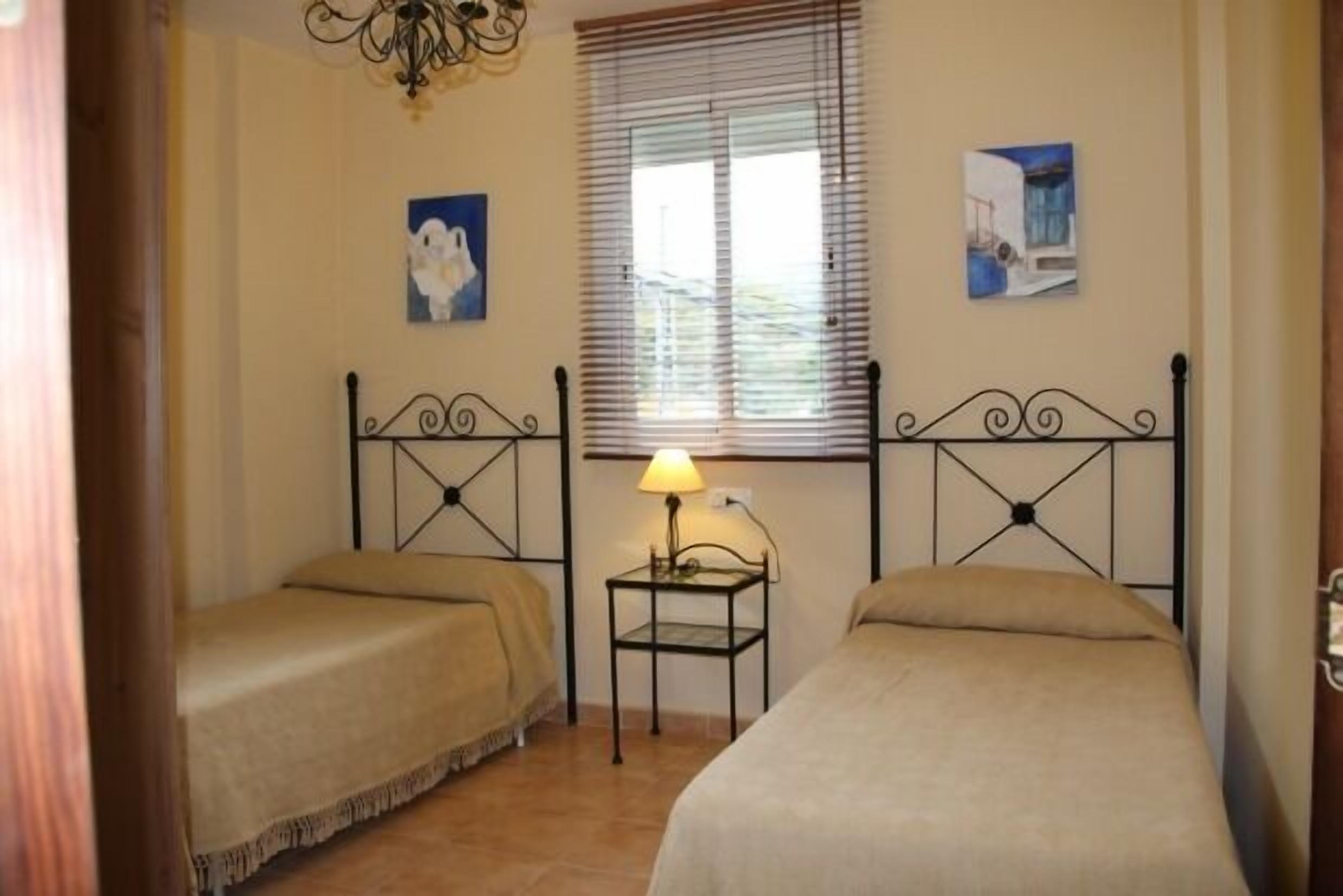 Une chambre avec deux lits, une petite table avec une lampe et deux tableaux accrochés au mur.