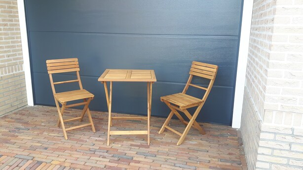 Dos sillas de madera y una mesita contra un muro azul, con suelo de ladrillo.