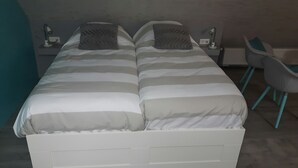 Una cama doble con ropa de cama a rayas, dos lámparas de noche y una silla con patas color turquesa.