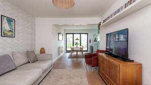 Una sala de estar moderna con sofá, un aparador de madera, televisor y comedor con mesa y sillas.