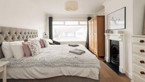 Un dormitorio con cabecera capitonada, una cama grande con una manta mullida, una chimenea y vistas al exterior.