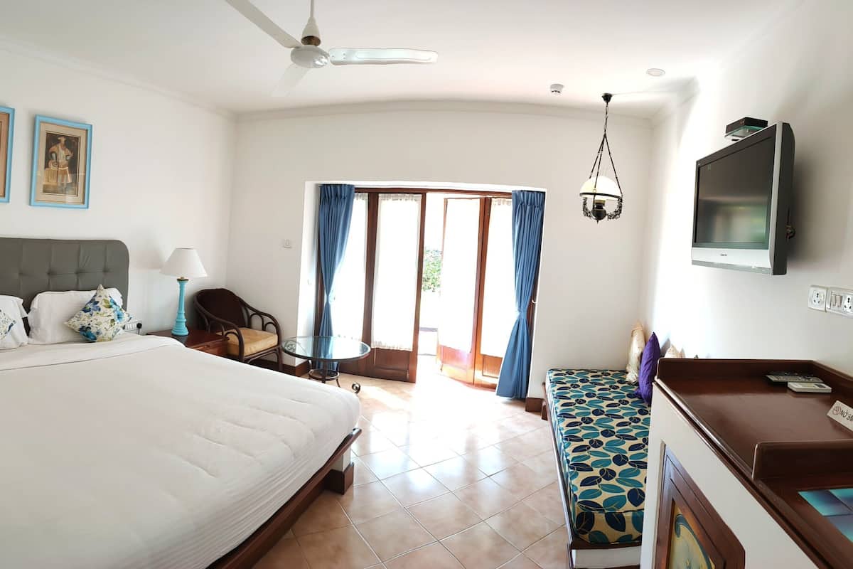 Habitación de hotel con una cama grande, un escritorio con televisor de pantalla plana, una silla, una mesa y un balcón con cortinas.