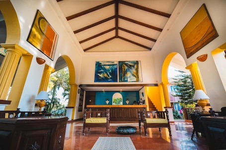 A lobby with a high ceiling, wooden beams, and a reception desk. There are two large paintings on the wall above the desk.