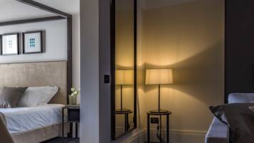 Habitación de hotel con cama, zona de estar, una silla, una mesa, una lámpara y un espejo grande.