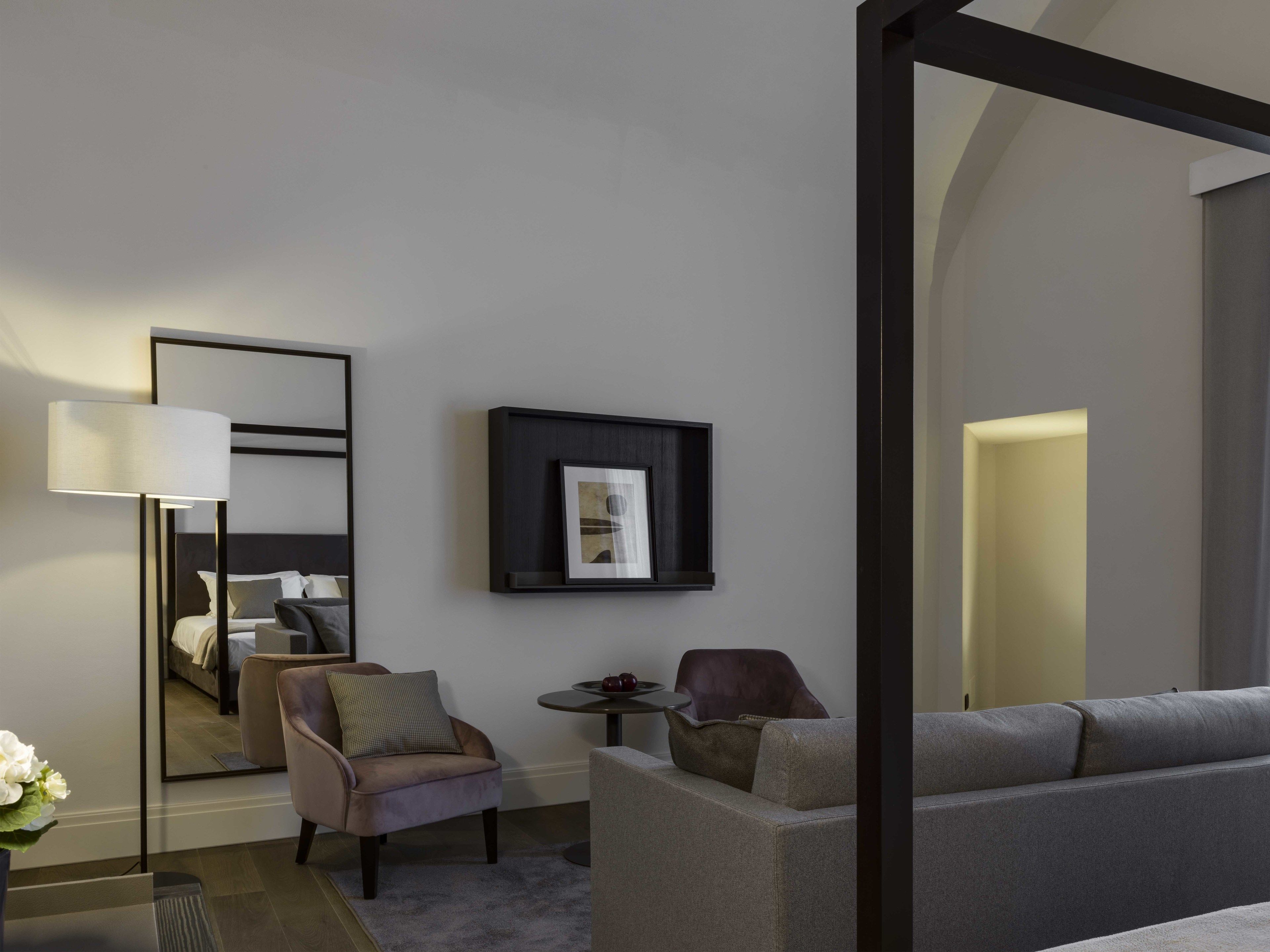 Une chambre d’hôtel moderne dotée d’un grand lit, d’un coin salon avec un canapé et des fauteuils, d’une petite table ronde et d’un lampadaire.
