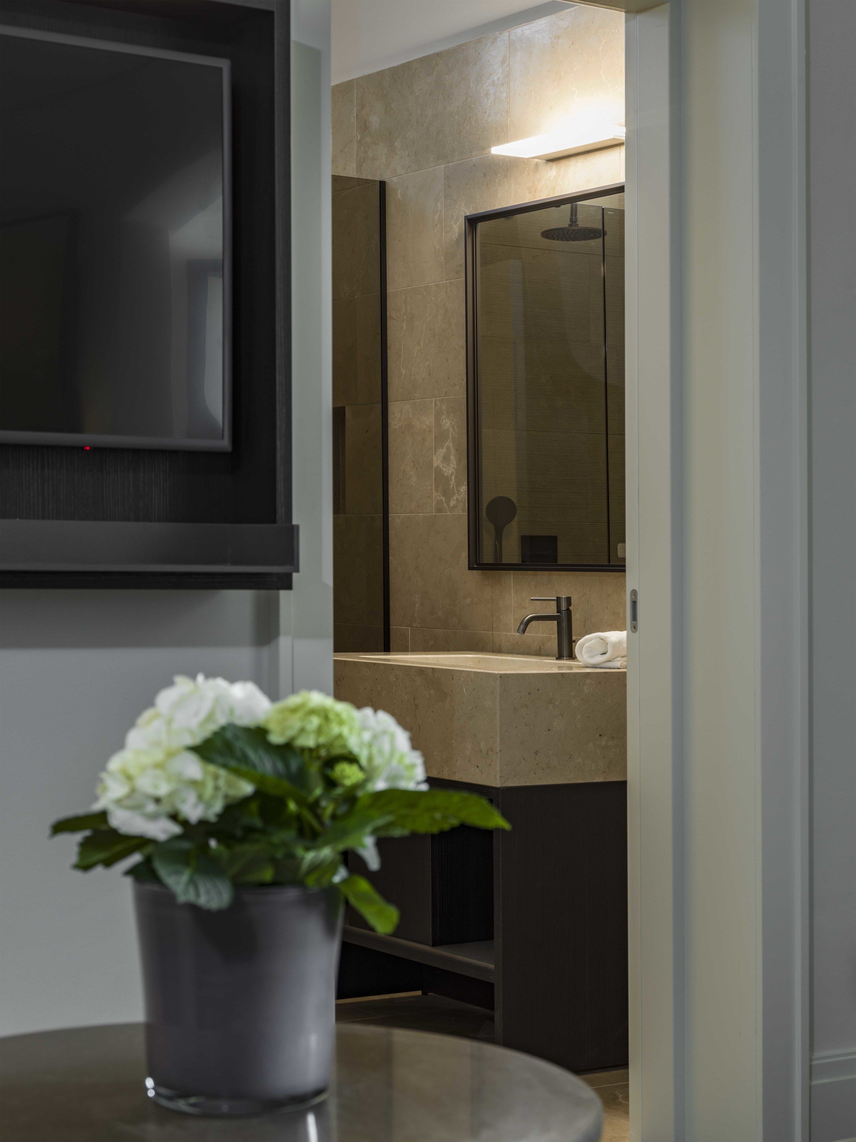 A modern bathroom with a large mirror, a sink, and a television mounted on the wall.