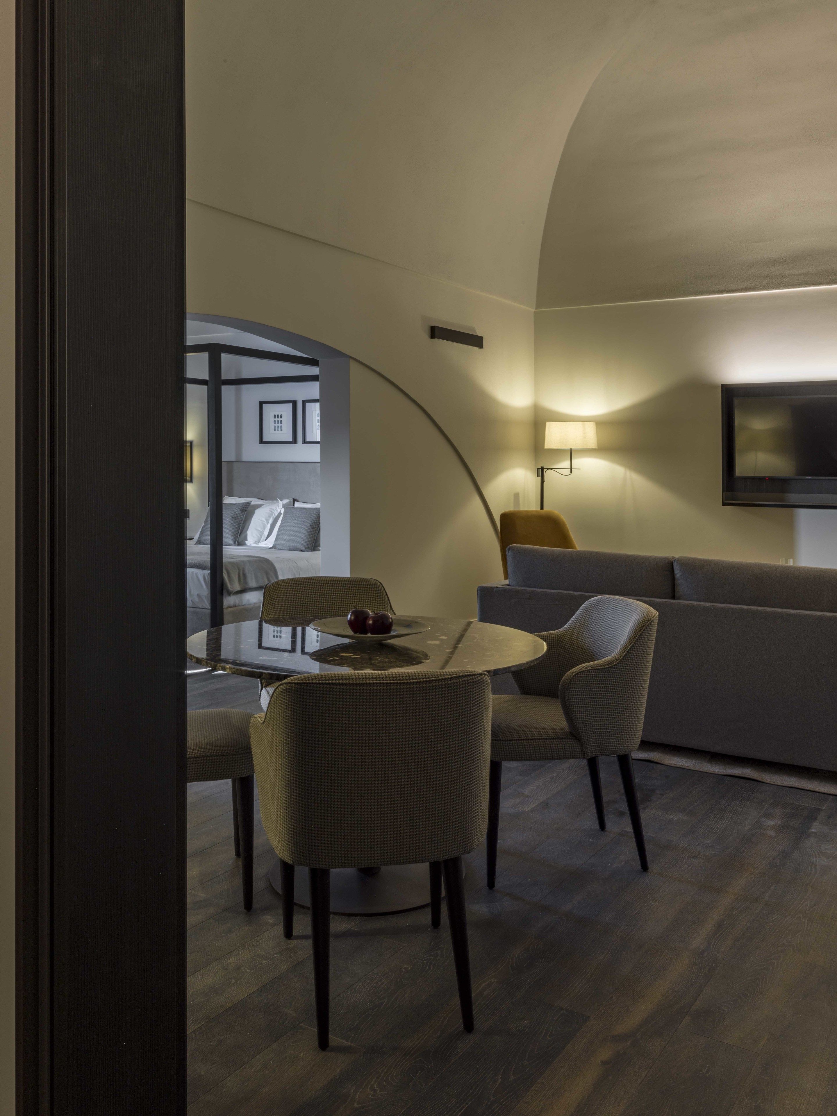 A modern living room with a curved ceiling, a round glass table, two upholstered chairs, a sofa, and a flat-screen TV mounted on the wall.