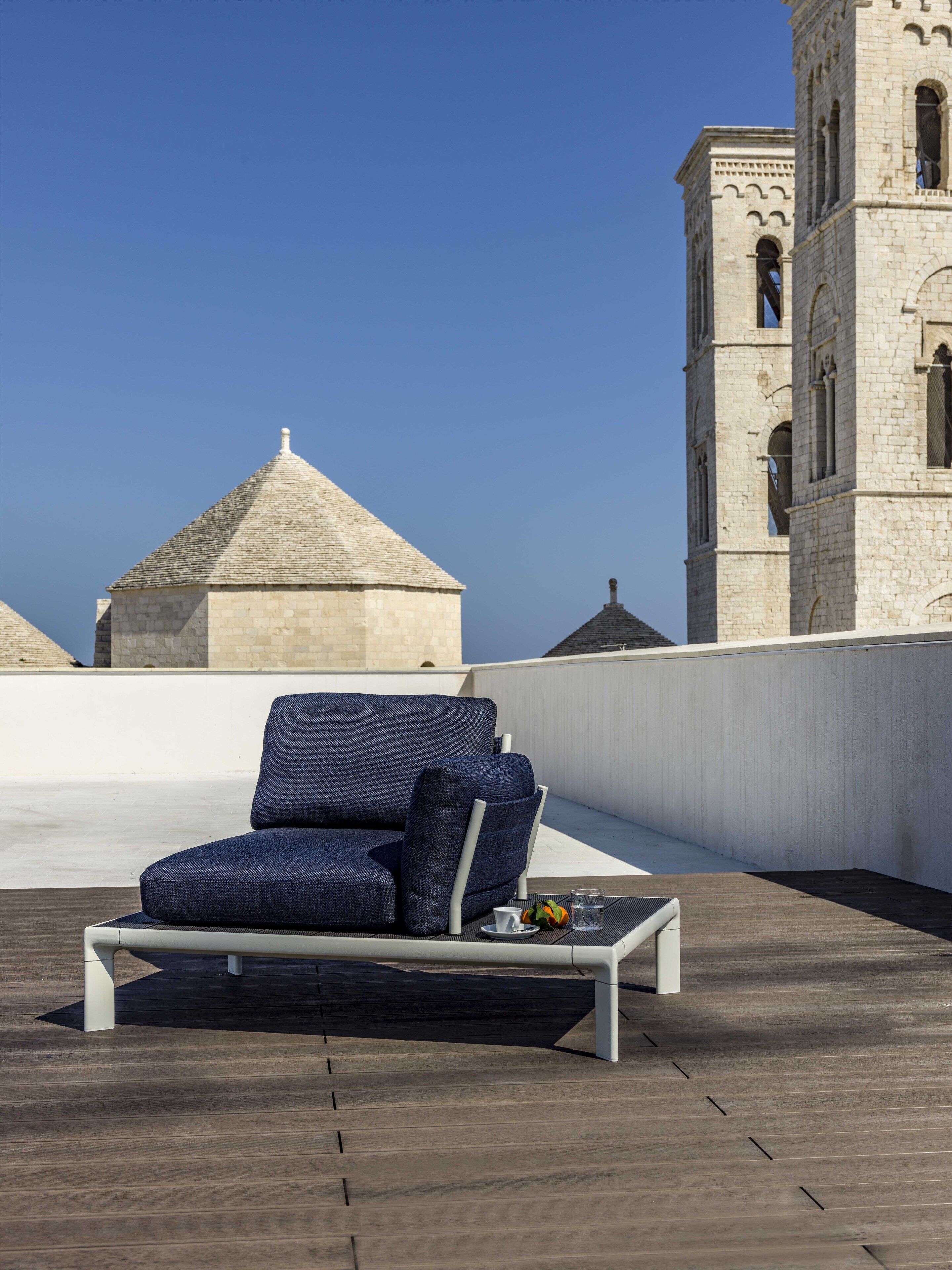 Une terrasse sur le toit, avec un canapé bleu et une petite table, d’où l’on peut admirer un bâtiment historique doté d’une tour.