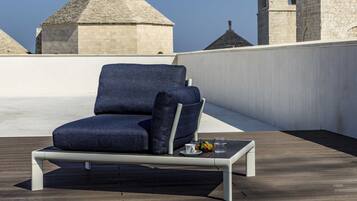 Eine Dachterrasse mit einem blauen Sofa und einem kleinen Tisch, mit Blick auf ein historisches Gebäude mit einem Turm.
