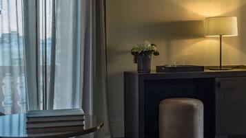 Habitación de hotel moderna con sofá, escritorio con lámpara, florero con flores y vistas a través de cortinas translúcidas.