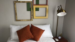 A neatly made bed with white and brown bedding, a bedside table with a clock and decorative items, and wall-mounted picture frames.
