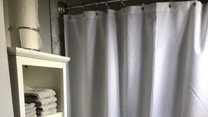 A room with a bed, a white curtain, and a towel hanging on a hook.