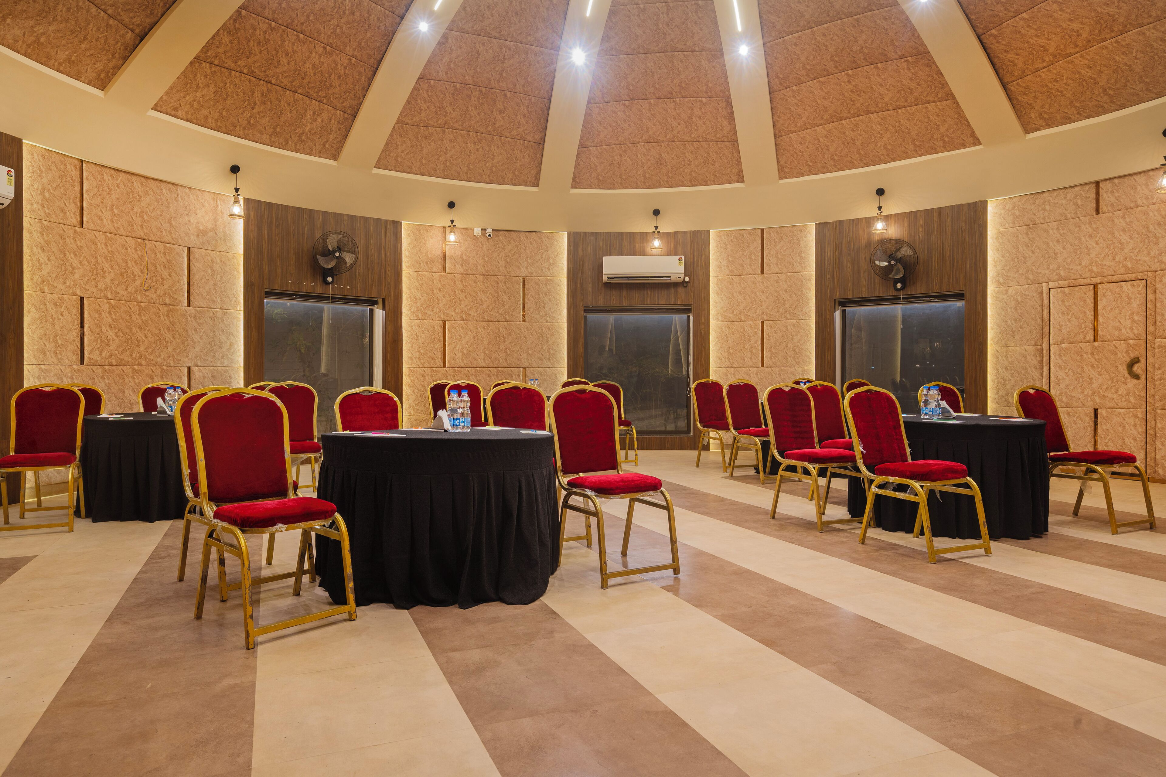 Un salón de conferencias con mesas redondas, sillas rojas y un techo alto con iluminación empotrada.