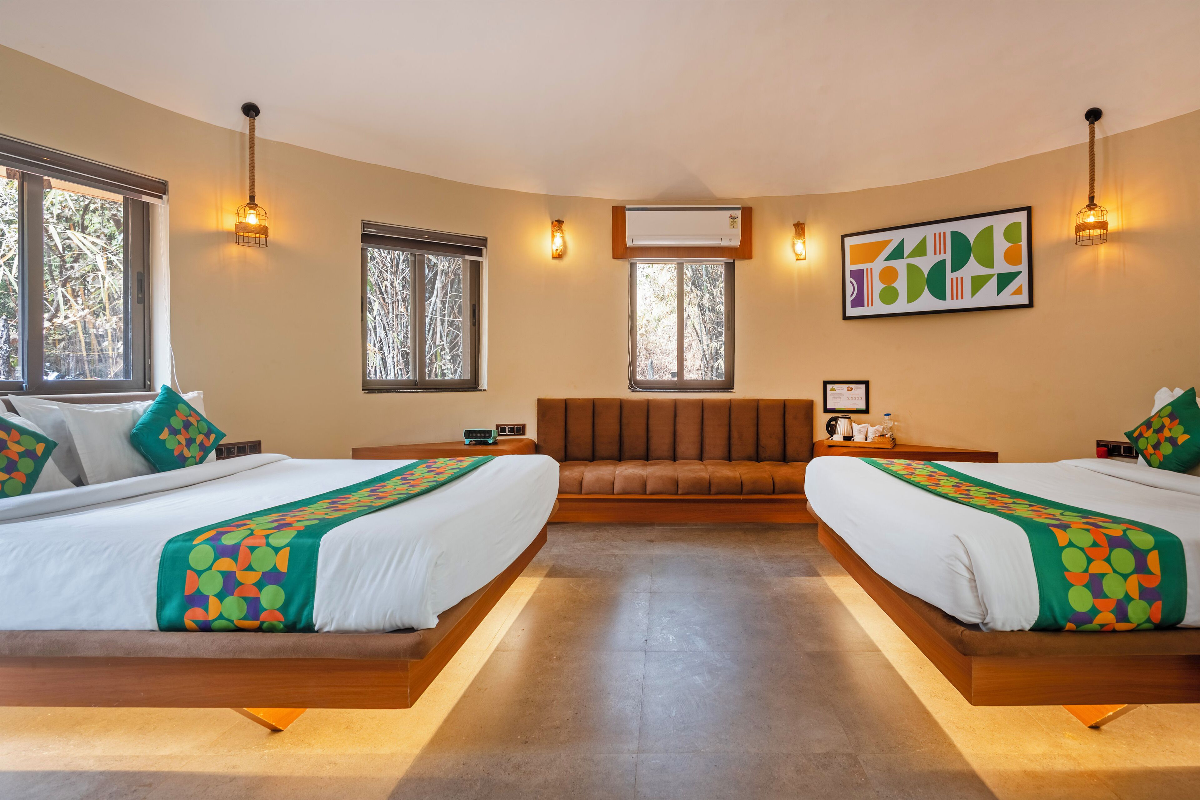 A hotel room with two beds, a sofa, a large window, and a wall-mounted air conditioner.
