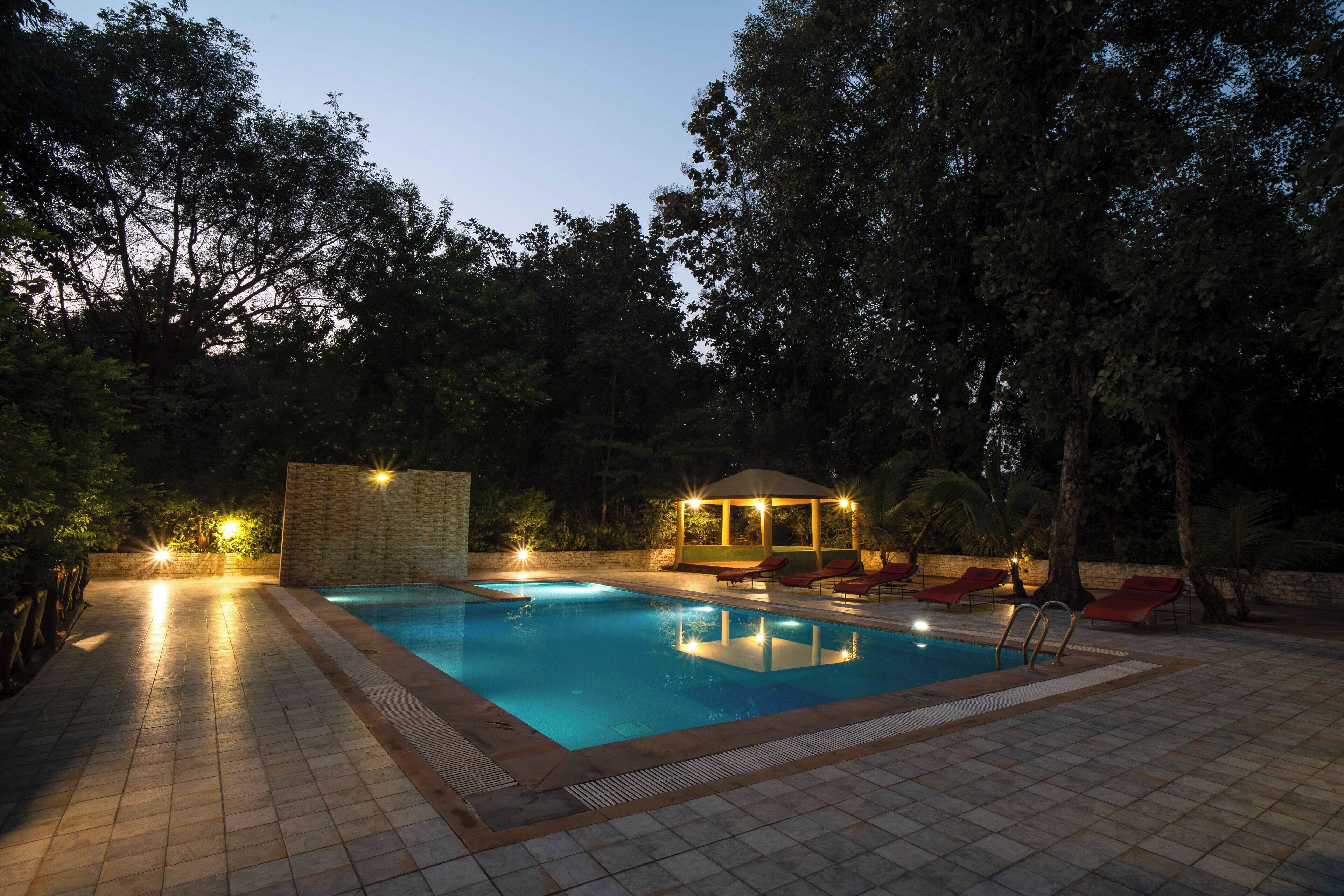 A swimming pool with a tiled deck, a gazebo, and red lounge chairs.