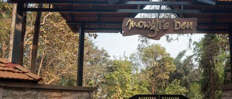 Un letrero de madera con el nombre "Mowgli's Den" colgado sobre una entrada con portón.