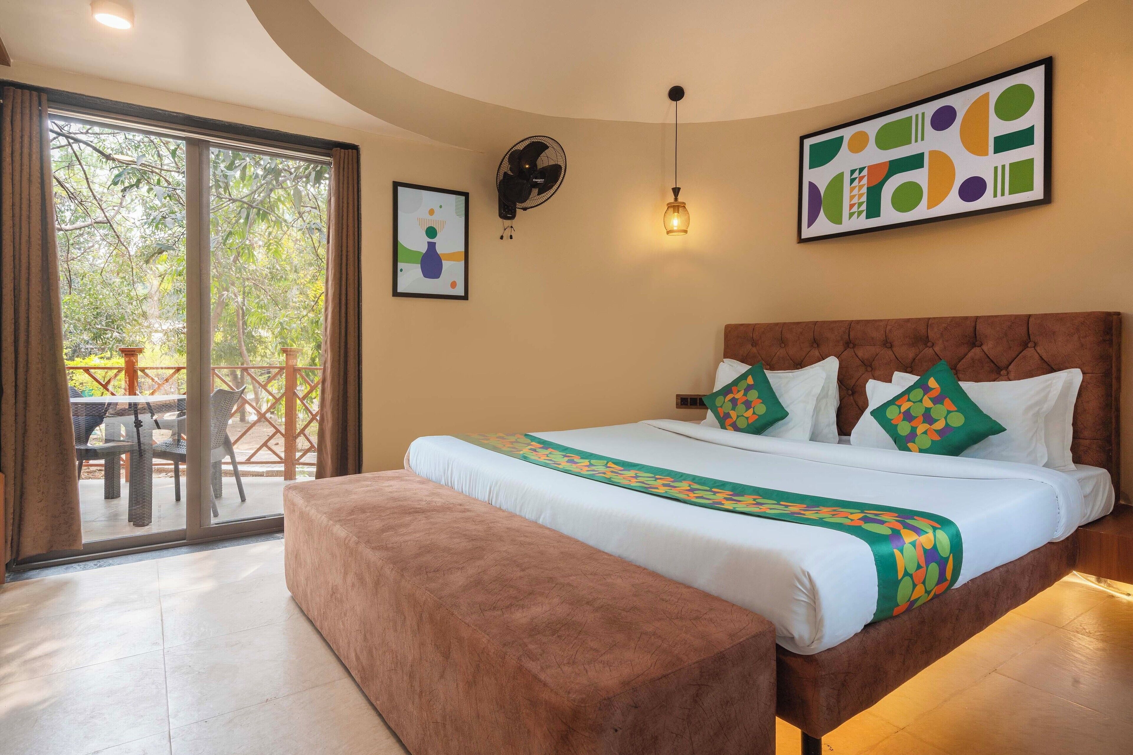 Un dormitorio con una cama grande, un banco, un ventilador, una mesa con sillas y vistas al exterior.