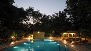 Una piscina con bordeado de baldosas, un pabellón y sillas de descanso.