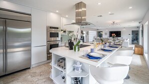 Uma cozinha moderna com eletrodomésticos de aço inoxidável, uma ilha central com bancos e uma janela grande que proporciona luz natural.