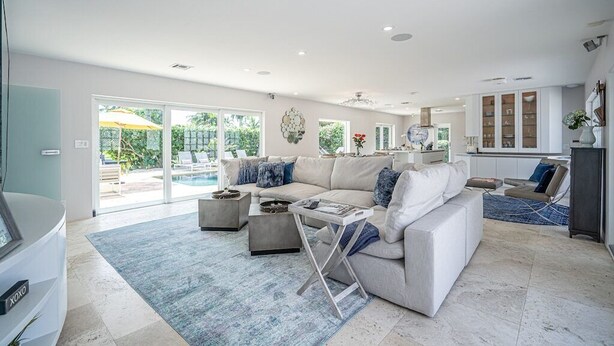 Uma sala de estar ampla, com um sofá grande, mesa de centro e vista para uma piscina através de portas de vidro.