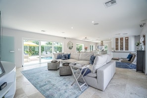 Un salon spacieux avec un grand canapé, une table basse et une vue sur une piscine, visible à travers des portes vitrées.