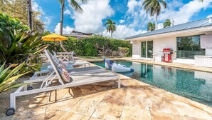Uma área de piscina moderna com espreguiçadeiras, um pequeno bote inflável e uma churrasqueira.