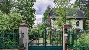 A gated entrance to a property with a traditional design, featuring a green iron gate and a white building with a dark roof. - Villa Ariane Saint-Jorioz (Saint-Jorioz)