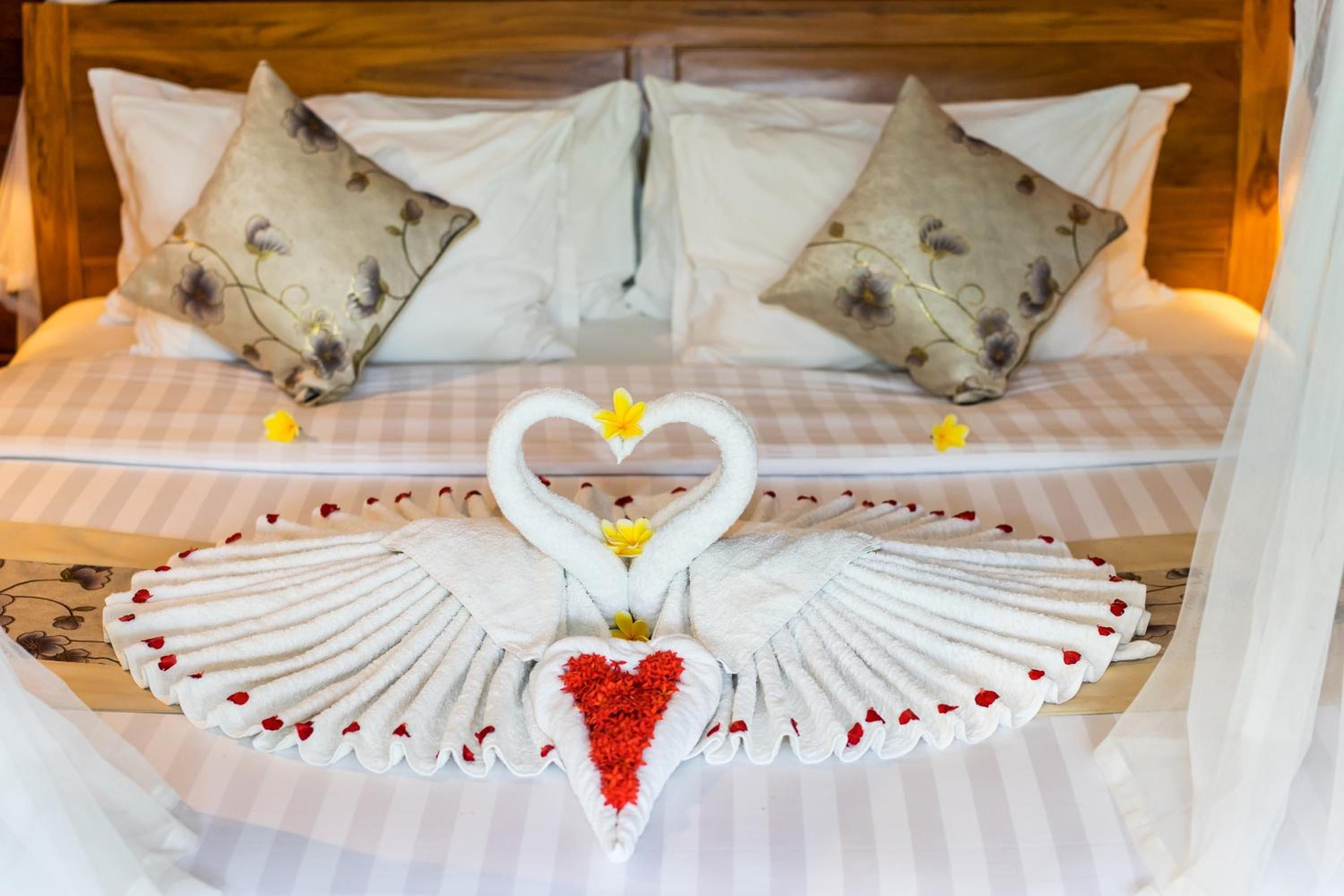 A bed with a checkered bedspread, two pillows with a floral pattern, and a decorative swan towel arrangement with a heart in the center.