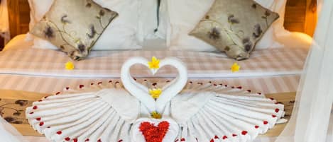 A bed with a checkered bedspread, two pillows with a floral pattern, and a decorative swan towel arrangement with a heart in the center.