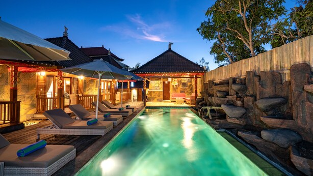 A swimming pool with lounge chairs and umbrellas, surrounded by a wooden deck and stone walls. - Royal Cottage Nusa Lembongan (Lembongan Island)