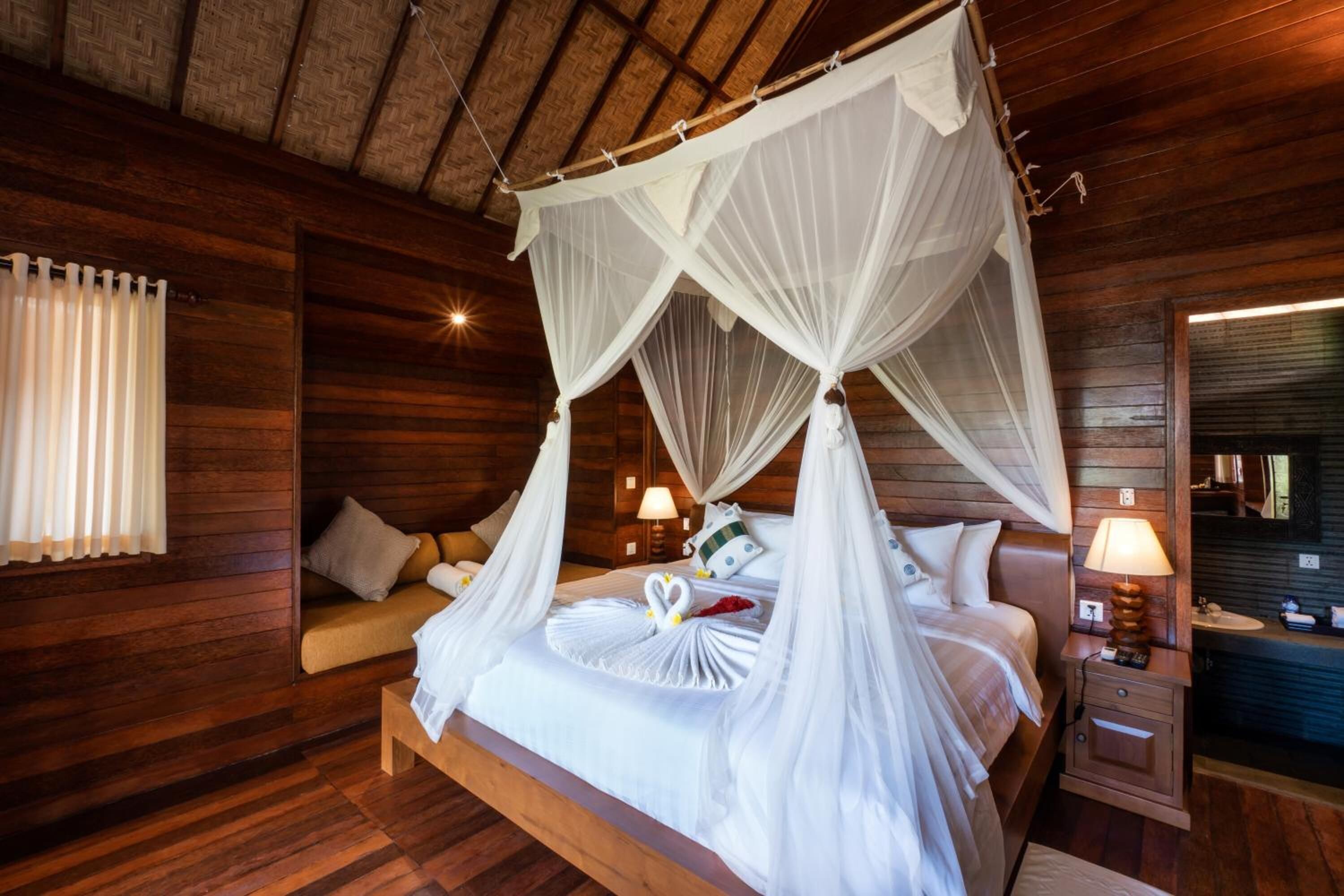 Une chambre à coucher de style cabane en bois, avec un lit à baldaquin, une table de chevet avec une lampe et une fenêtre avec des rideaux.