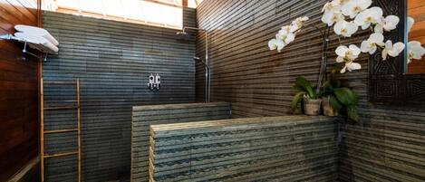 A bathroom with a wooden ceiling, a bamboo ladder, a towel rack, a sink, a mirror, and a potted plant.