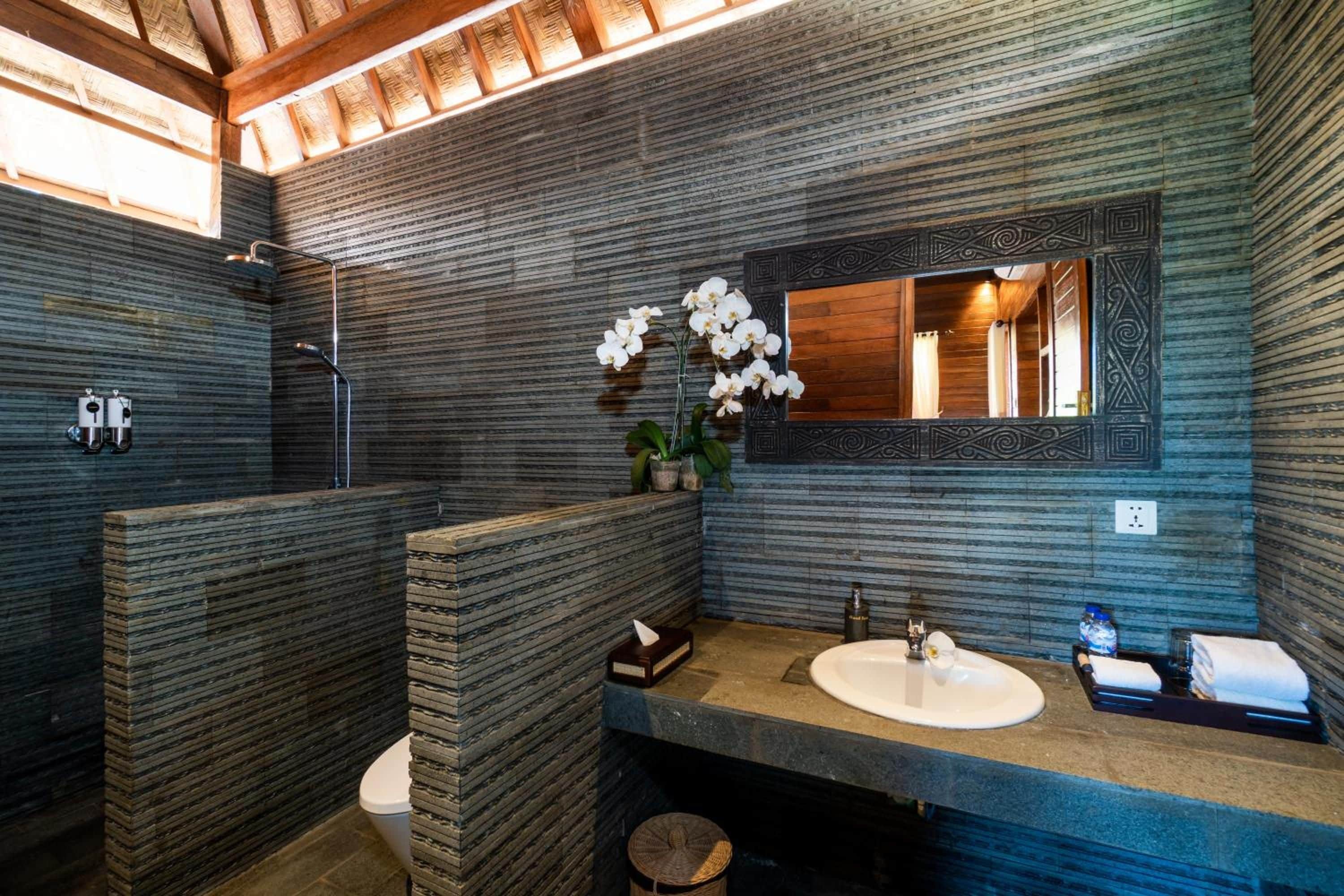 Un baño moderno con diseño de pared de piedra, un lavabo, un inodoro y una zona de ducha.