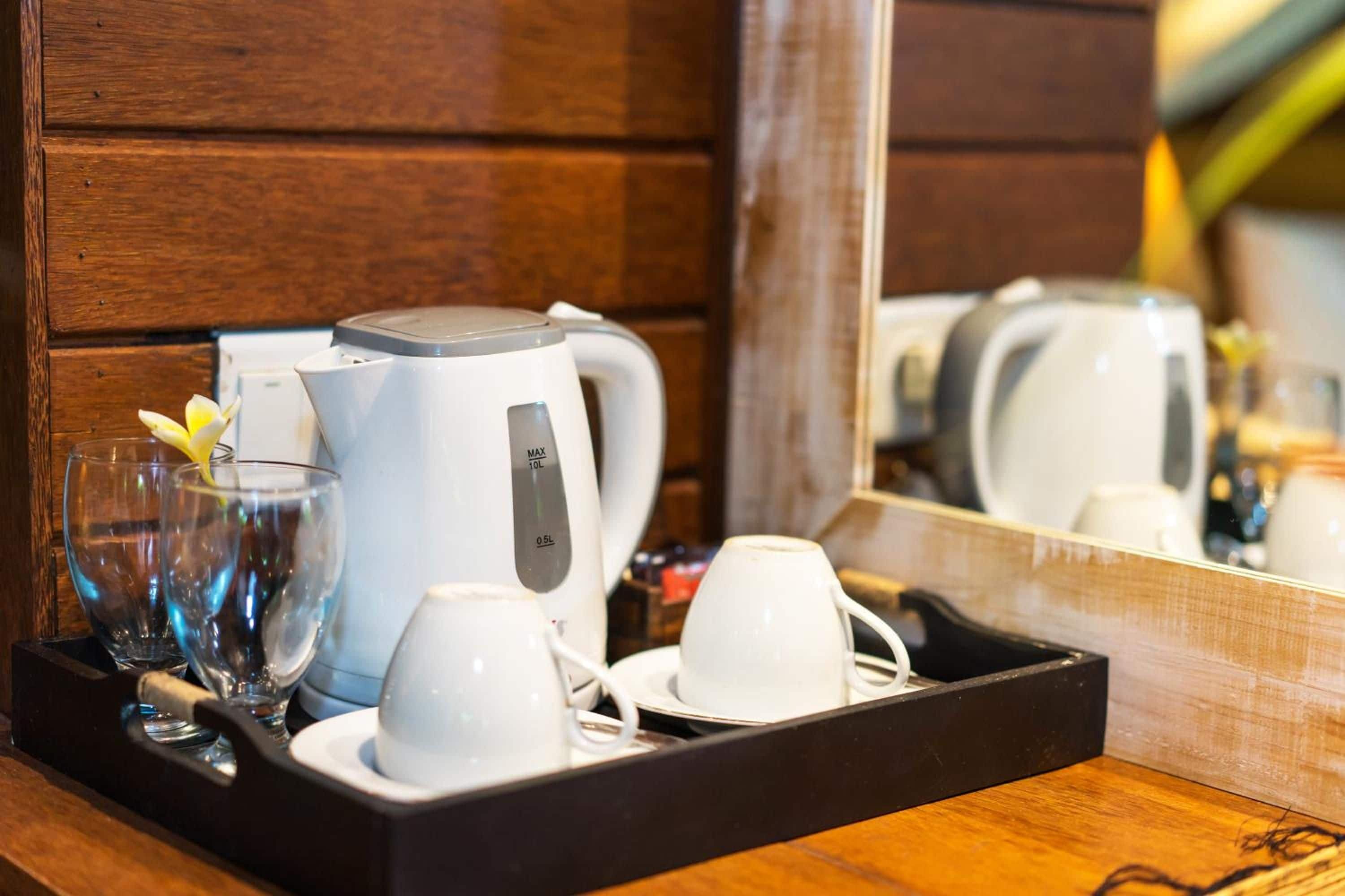 Een dienblad met een koffiezetapparaat, twee kopjes en een glas met een bloem.