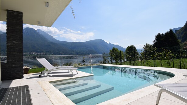 Una piscina con escalones de acceso, rodeada de un patio con sillones de descanso.