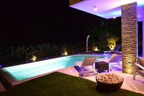 Una piscina con dos sillas de descanso y un pilar de piedra, rodeada de un patio bien iluminado.
