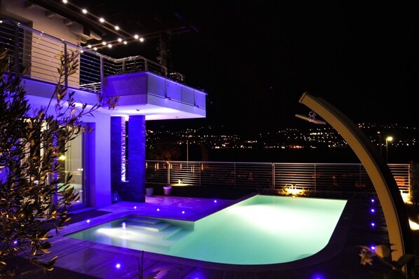 Un área de piscina moderna al aire libre con vista a la ciudad de noche.