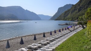 Un resort junto al lago con hileras de tumbonas y sombrillas a lo largo de la orilla, rodeado de montañas.