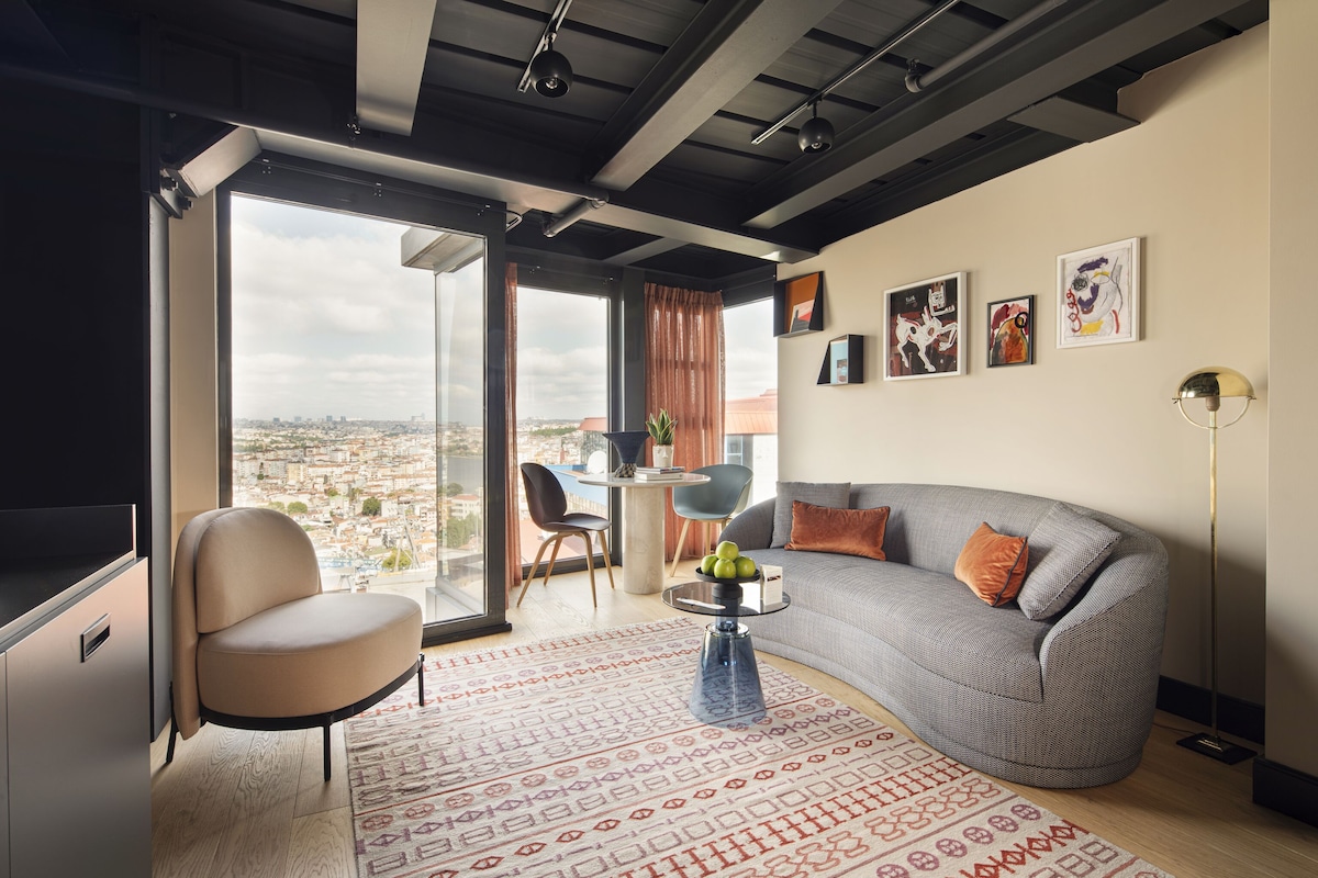 Ein modernes Wohnzimmer mit einer gebogenen grauen Couch, einem runden Couchtisch und einem großen Fenster mit Blick auf die Stadt.