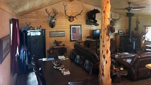 L’intérieur d’un chalet rustique, avec des murs en bois, un coin repas comprenant une table et des chaises, une cheminée et des têtes d’animaux fixées au mur.