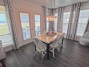 Uma área de refeições com mesa e cadeiras de madeira, um lustre e cortinas estampadas.