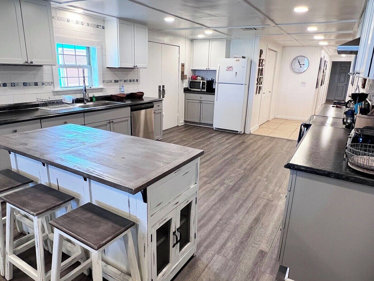 Uma cozinha moderna com uma ilha central, banquetas, micro-ondas, frigorífico e um relógio na parede.