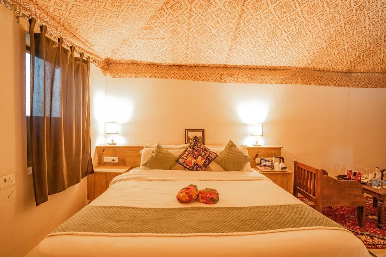 Una habitación de hotel con una cama grande, dos mesitas de noche, una silla de madera y un techo con diseño.